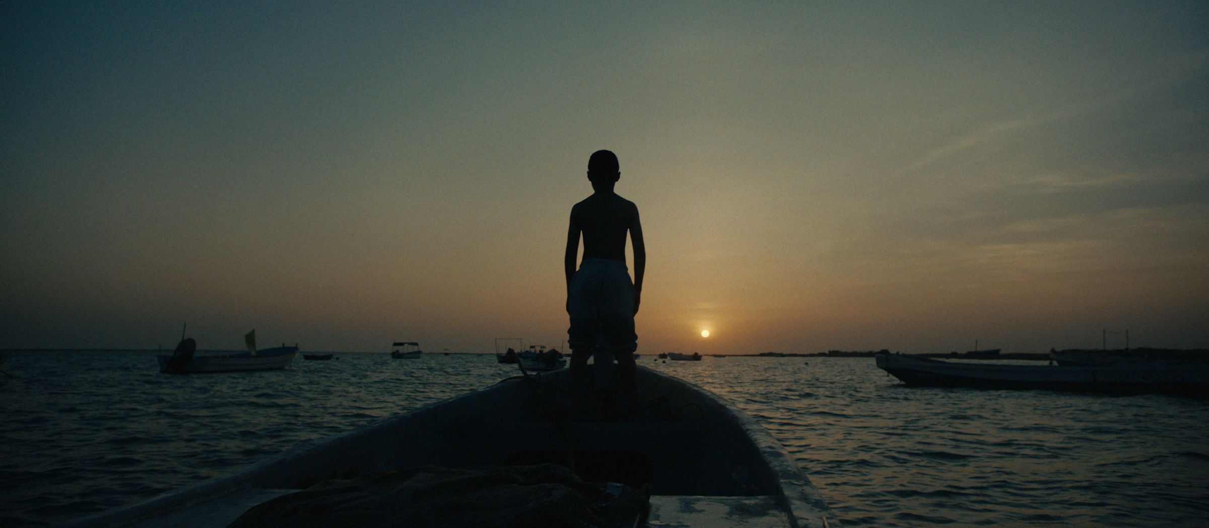A boy at the bow of a boat at sunset